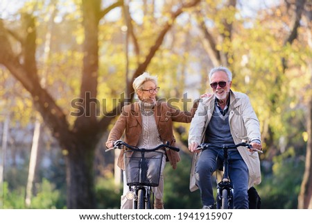 Cheerful active senior couple with bicycle in public park together having fun. Perfect activities for elderly people. Happy mature couple riding bicycles in park Royalty-Free Stock Photo #1941915907