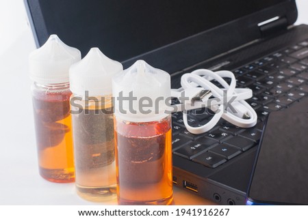 Old smartphone, USB cord, laptop and liquid for electronic cigarettes, casually lying on the table. Electronic equipment for work and communication. Items on a gray isolated background.