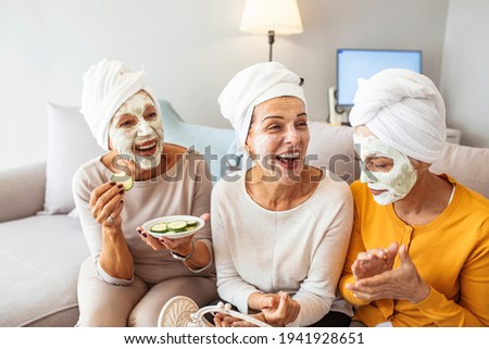 Three mature happy women with face masks at home. Friendship and wellbeing concept. Pretty mature female friends having spa day. Natural homemade facial mask. 