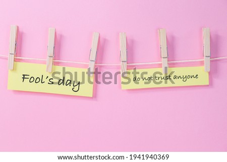 Yellow papers with a fool's day message hang on a clothesline with wooden clothespins on a pink background, close-up side view.