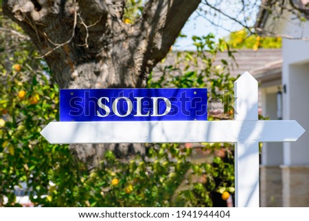 Sold real estate sign on wooden post. Blurred green landscaping background