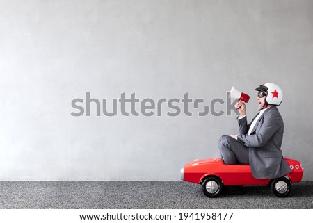 Senior man riding toy car. Full length portrait of funny businessman against concrete wall with copy space. Business start up concept