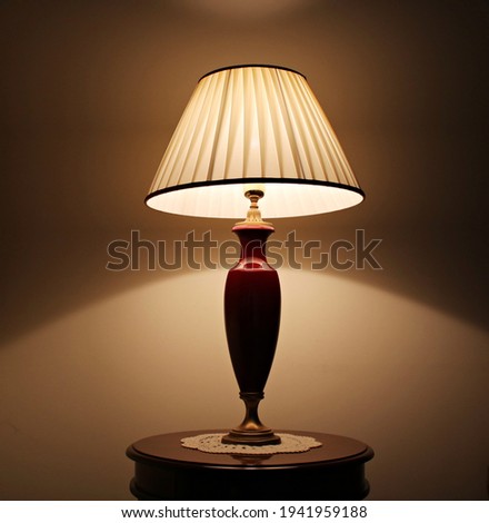 Coassic elegant lamp with illuminated lampshade on a small round table in the room. Royalty-Free Stock Photo #1941959188