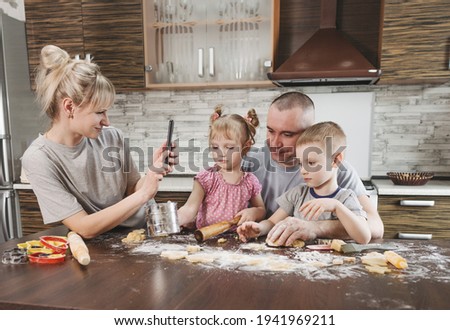 happy mom takes pictures of dad with two young children in the kitchen while making flour cookies. happy family cooking together
