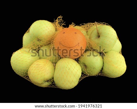 Apples and orange in a grid isolated on black. Ripe fruits in a string bag. Citrus with a picture of a cheerful face. Concept: joy, happiness, positive, individuality.