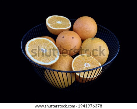 Oranges in a vase with other fruits. Ripe fruits in a bowl isolated on black. Citrus with a picture of a cheerful face. Concept: joy, positive, happiness, smile