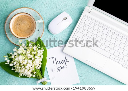 Notes thank you, coffee cup, laptop, bouquet of flowers lily of the valley on desk. Workplace in home office laptop and thank you note. Thankfulness, customer service, thanks card concept

