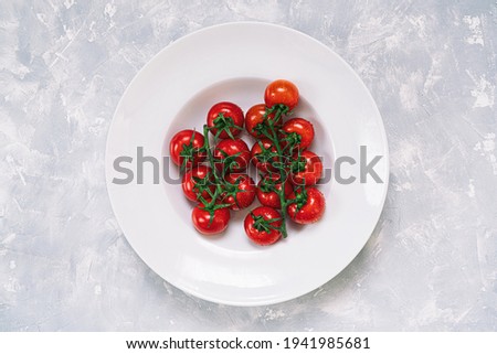 Red Cherry Tomatoes On White Plate with white marble background.Top view with copy space.
