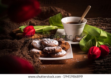 Lifes. Tea and biscuits, still: Rustic. On the table are red tulips and linseed. The biscuits are sprinkled with the icing sugar.Lifes. Tea and biscuits, still: Rustic. On the table are red tulips and
