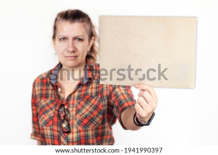 Middle aged woman in work clothes holds a sheet of cardboard without any inscription. Copy space. Isolated. Woman with a sign in her hands