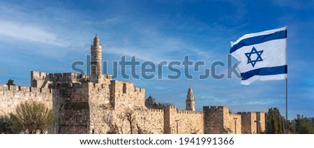 Panorama of Jerusalem's Citadel near the Jaffa Gate with Tower of David, ancient fortress walls and Israeli flag. Zion Mount with buildings of Dormition Abbey and bell tower on background. Royalty-Free Stock Photo #1941991366