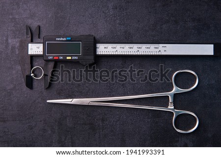Electronic caliper with piercing earring and clips. Lying on a black background. Piercing theme