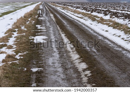 Mud field road running through snowy fields in late winter