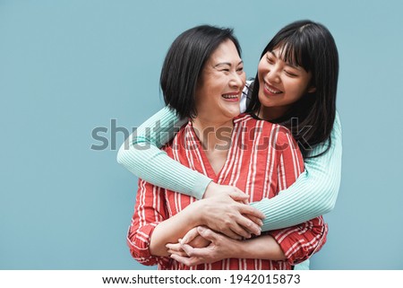 Asian mother and daughter hugging outdoors with blue background - Main focus on right female face Royalty-Free Stock Photo #1942015873
