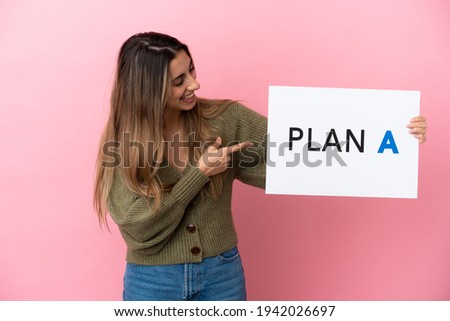 Young caucasian woman isolated on pink background holding a placard with the message PLAN A and  pointing it