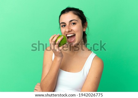 Young caucasian woman isolated on green background eating an apple