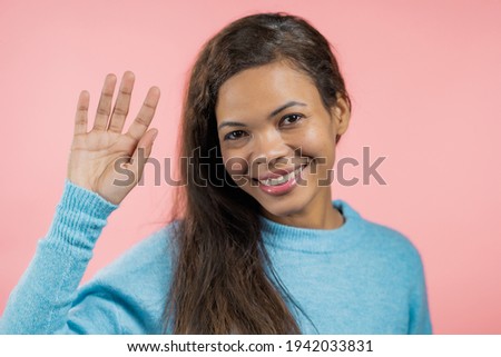 African friendly woman waving hand - hello. Greeting, say Hi to camera. Beautiful mixed race lady on pink studio background. 