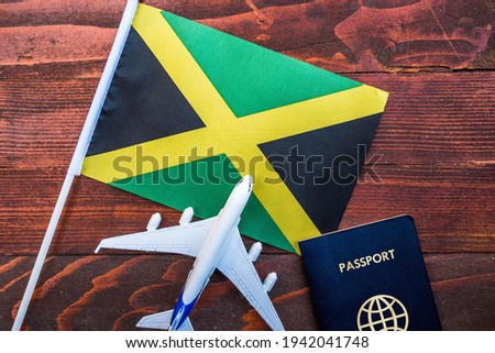 Flag of Jamaica with passport and toy airplane on wooden background. Flight travel concept.