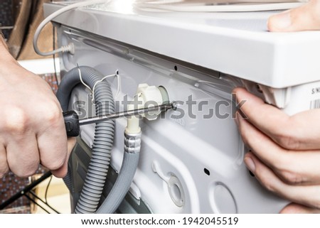 handyman repair washer at back side. washing machine repair service concept. connecting water supply to appliance. Royalty-Free Stock Photo #1942045519