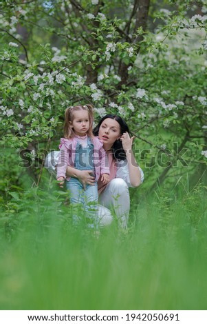 Mom and little daughter in white flowering branches of apple trees in spring
