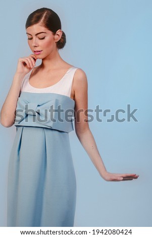 American shot of beautiful stylish fashion girl in blue dress looking down. Isolated on blue background. Design copy space.