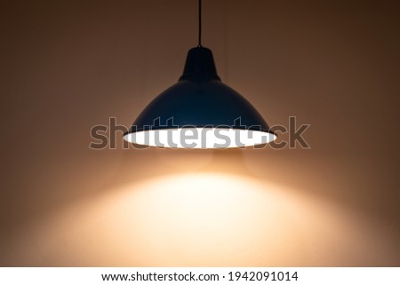 A classic ceiling electric lamp during glowing with warm light color shade on the room wall. Selective focus at the lamp's edge part. Photo contain high contrast and noise of dark area.