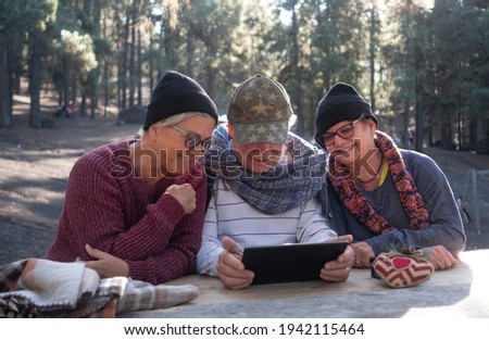 Smiling group of friends enjoying technology and social media sitting outdoors at a wooden table using a digital tablet