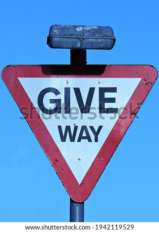Weathered street sign, inverted triangle shape, on which words "GIVE WAY" are printed in black capital letters on white background  Red border around