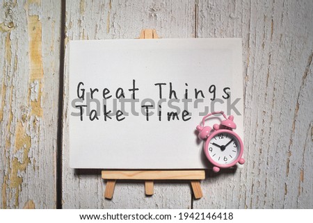 Motivational wording Great Things Take Time with clock and white board over a wooden background with flare effect. Motivational concept