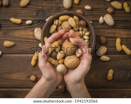 The girl is holding a lot of different nuts on the background of the table. Vegetarian food.