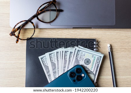Business concept. Laptop, banknotes of us dollars, business card holder, smart phone and opened Notepad with pen. Top view of the texture of expensive wood.
