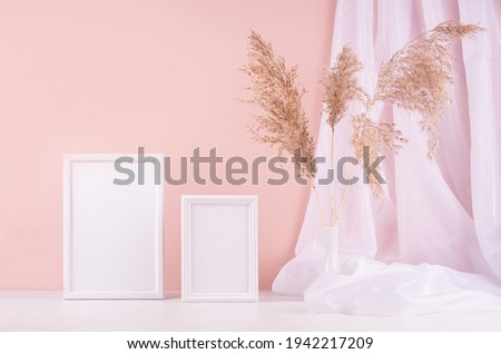 Calm home decor with set of two blank photo frame for text, design, poster, silk curtain, fluffy reeds on white wood table, pink wall. Template for display and portfolio.