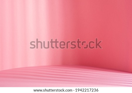 Soft light pastel pink background with glowing sunlight through jalousie and striped shadows on wall and floor. Tender beauty scene for showing, display and presentation.