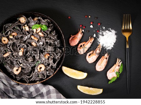 black pasta and Shrimps with salt and lemon in a frying pan on a black background