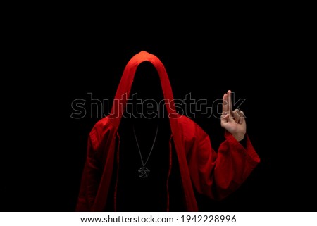 Mystery man in a red hooded cloak in the dark. Unrecognizable person. Hiding face in shadow. Pointing up with fingers. Ghostly figure. Sectarian. Conspiracy concept.

 Royalty-Free Stock Photo #1942228996