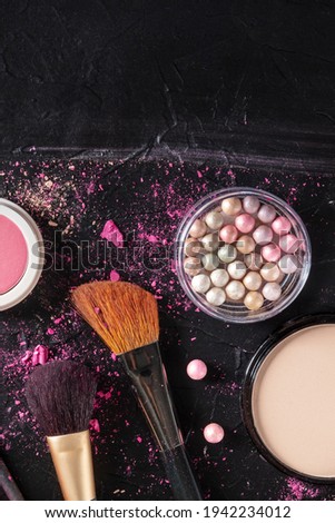Make-up brushes, pearls, powder, shot from above on a black background