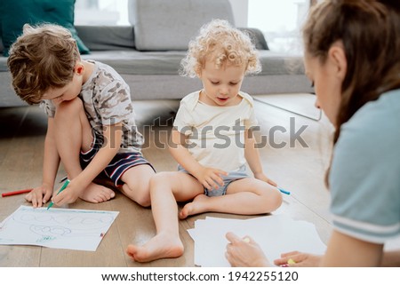 Portrait of siblings, a school-aged boy and a preschool-aged girl sitting on a wooden floor in the living room at home and painting with colored markers.