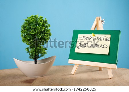 Opportunities just ahead written on a sticky note on a mini green notice board with a plant with blue background