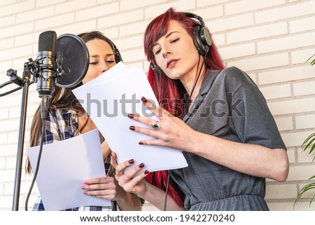 From below young female hostesses reading script before recording radio podcast in studio