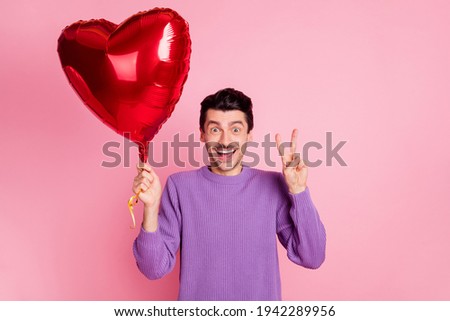 Portrait of attractive cheerful guy holding heart air ball showing v-sign isolated over pink pastel color background