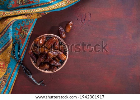 Bronze plate with dates and  tasbih (misbaha) on old red-brown wooden table. Ramadan background.  Flat lay. Selective focus. Royalty-Free Stock Photo #1942301917