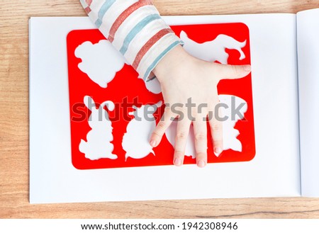 Children's hand holds a stencil on the background of the sketchbook. Early baby development concept.