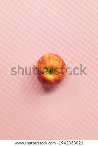 In the vertical photo in the center on a pink background lies one ripe apple of the gala variety. An apple in the skin. The apple is whole.