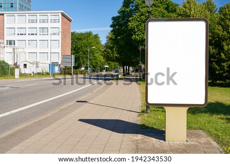 Empty city light poster as an advertising mock-up template next to street and sidewalk in summer