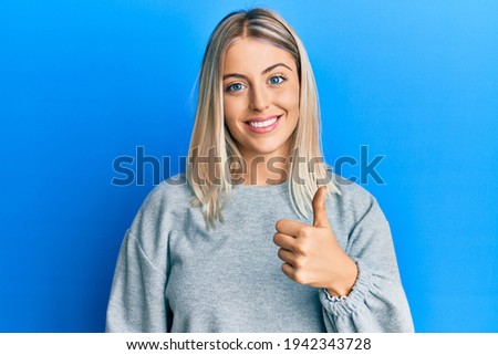 Beautiful blonde woman wearing casual clothes doing happy thumbs up gesture with hand. approving expression looking at the camera showing success. 