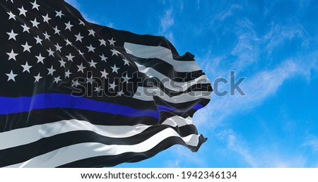 Thin Blue Line. Black Flag of USA with Police Blue Line waving in the wind on flagpole against the sky with clouds on sunny day