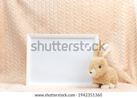 Close-up of empty white frame without picture. Cute childs toy near framework. Concept of childhood, play, studio decoration and friendly atmosphere, copyspace