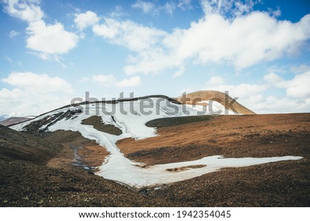 Sunny mountain desert relief with glacier in sunlight under blue cloudy sky. Scenic highlands landscape with small glacier high in mountains on hills. Minimalist mountain scenery of highland desert.