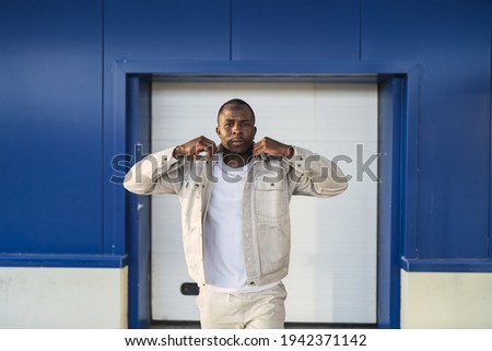 A closeup shot of a young Black male standing outdoors in front of a blue and white wall