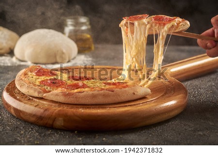A hand grabbing a slice of delicious cheesy pepperoni pizza with a wooden spatula